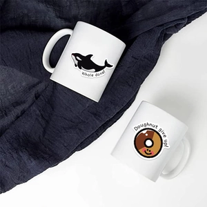 Close-up of two ceramic mugs with creative Whale done and Doughnut give up illustrations