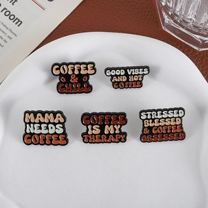 Five coffee-themed enamel pins with slogans on a ceramic plate with leather background