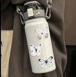 Drie kleurrijke vlinderstickers op een crèmekleurige thermosfles in een lifestyle-setting
