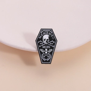 Gothic coffin enamel pin with Memento Mori skull and wings on a white ceramic plate