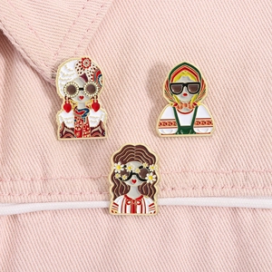 Détail de trois broches en émail de filles à la mode sur un fond en jean rose
