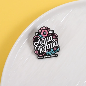 Black Aqua Tofana enamel pin with pink floral detail on a white ripple ceramic tray