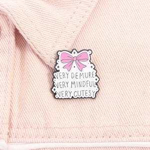 Detail of pink bow enamel pin with 'Very Demure' text on pink denim fabric background