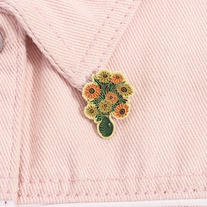 Detailed enamel brooch featuring sunflowers in a vase on a pink denim jacket