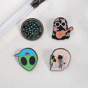 Detailed close-up of four enamel pins with ghost, alien, and skeleton motifs on canvas