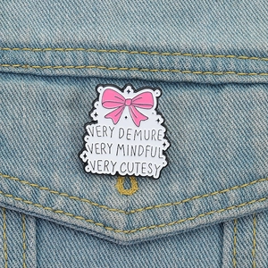 Pink bow enamel pin with Very Demure slogan on a denim jacket pocket
