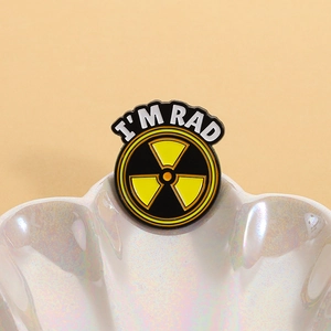 Gros plan du pin's émaillé symbole radioactif I'M RAD sur un plateau en nacre irisée