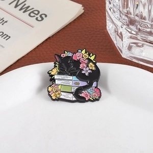Detail of a black cat enamel pin sleeping on books with colorful floral accents