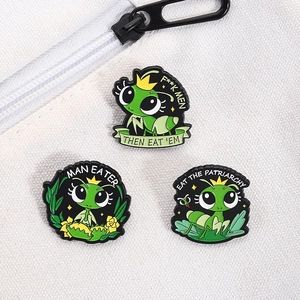 Close-up of three cartoon green mantis enamel pins with feminist slogans on white canvas