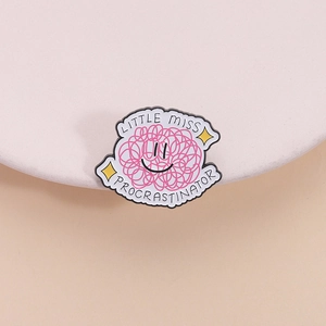 Detailed close-up of a pink enamel pin featuring a smiley face and Procrastinator quote