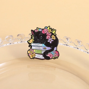 Detailed close-up of a black cat enamel pin resting on colorful books with floral accents