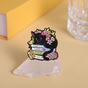 Macro shot of sleeping black cat enamel pin on colorful books with floral details