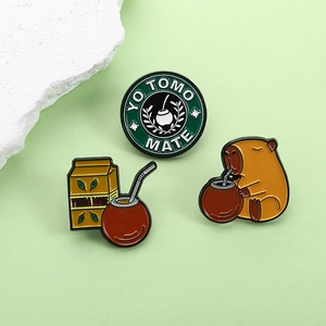 Three-piece enamel capybara and yerba mate metal brooch set on a light green background