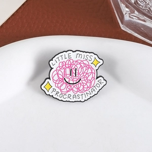 Pink enamel brooch with Little Miss Procrastinator lettering on a white ceramic plate