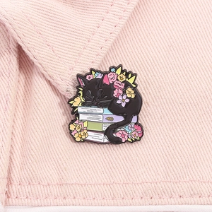 Detail of cartoon black cat sleeping on books enamel pin on pink fabric background