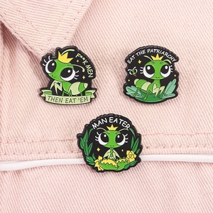 Detailed view of three green mantis enamel pins with crown on pink fabric background