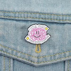 Little Miss Procrastinator enamel brooch on denim jacket with cartoon smiley face
