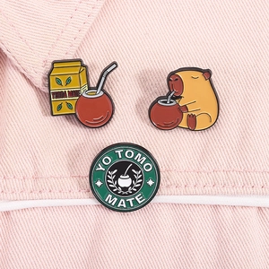 Close-up of enamel Capybara and Yerba Mate brooches pinned on pink denim jacket decor