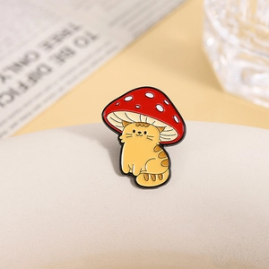 Détail d'une épinglette de chat jaune portant un chapeau champignon rouge en émail coloré