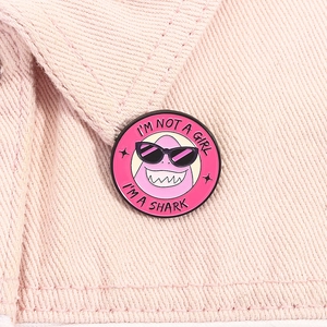 Détail d'un pin's émaillé requin rose sur denim avec slogan 'I'M NOT A GIRL I'M A SHARK'