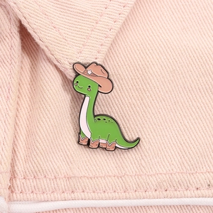 Detail of cartoon green dinosaur enamel pin wearing cowboy hat on pink denim fabric
