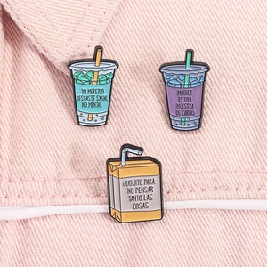 Drei farbenfrohe Emaille-Pins mit Cartoon-Getränkemotiven auf einer rosa Jeansjacke