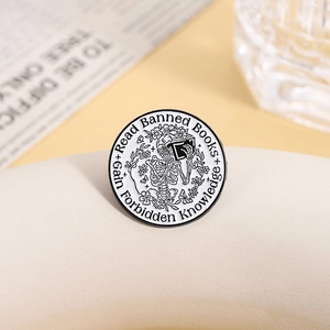 Round enamel pin featuring a skeleton reading books with floral and butterfly accents