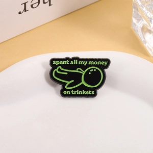 Pin de esmalte con gracioso personaje verde y frase sobre baratijas en plato blanco