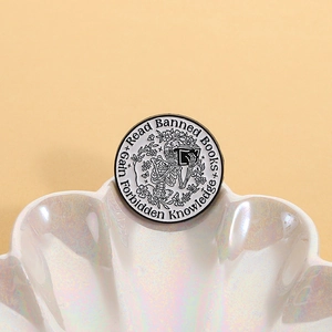 Skeleton reading book enamel pin with Read Banned Books slogan on shell display tray