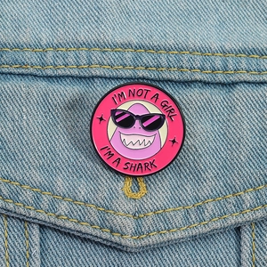 Pin's émaillé requin rose avec slogan sur une poche de veste en jean bleue
