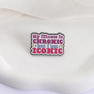 Dettaglio spilla in smalto rosa con testo 'My illness is CHRONIC but I am ICONIC'