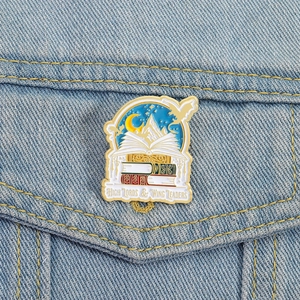 Fantasie Buch-Emaille-Pin mit Flügeln und Bergdesign auf blauem Jeanshintergrund