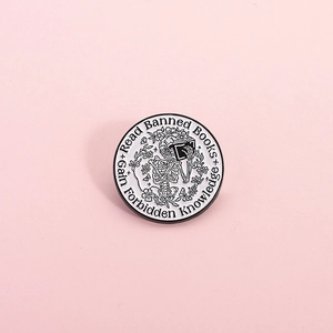 Round enamel skeleton pin reading banned books with floral accents and black white contrast