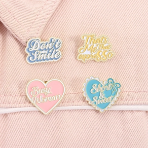Close-up of four colorful enamel pins with heart shapes and creative text on pink denim fabric