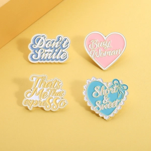Detail of four creative enamel pins with heart and letter slogans on yellow background