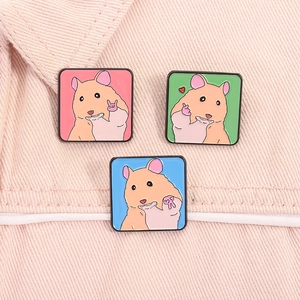 Détail de trois pins hamster en émail sur tissu denim avec des gestes mignons