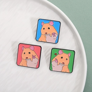 Trois pin's émaillés hamster colorés en bleu, rose et vert sur un plateau blanc