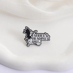 Minimalist black enamel dragon brooch with Faeries and Dragons text on a white tray