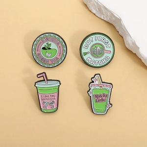 Close-up of four matcha themed enamel pins on a light yellow background with decorative stone