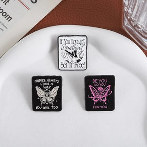 Set of three punk-style butterfly enamel pins with motivational quotes in a ceramic dish