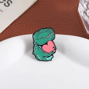 Cartoon green dinosaur enamel pin holding a pink heart on a decorative white plate
