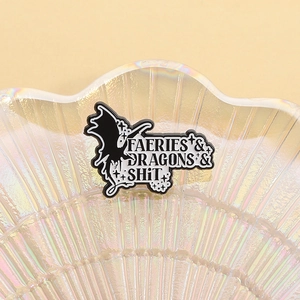 Detail of a cartoon dragon enamel pin with text displayed in a shiny shell tray