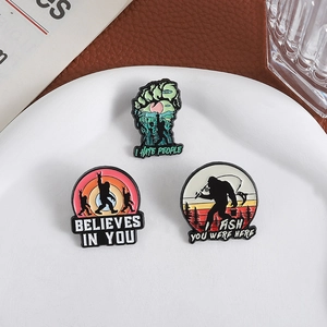 Three creative Bigfoot enamel pins with witty text slogans on a white ceramic plate