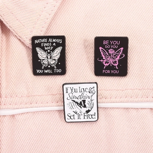 Detailed view of three enamel butterfly pins with inspirational quotes on pink denim fabric