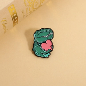 Cute cartoon green dinosaur enamel pin holding a pink heart on a warm desktop
