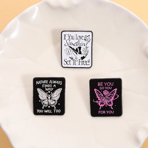 Set of three butterfly enamel pins with motivational quotes on a ceramic tray