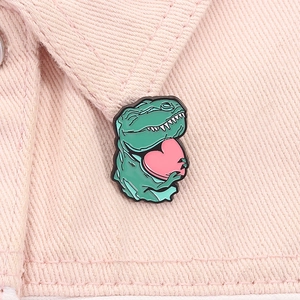 Nahaufnahme einer Emaille-Brosche mit grünem Dino und rosa Herz auf einem Jackenkragen