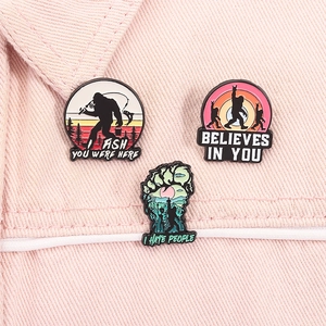Détail de trois épinglettes en émail Bigfoot avec thèmes de nature et pêche sur denim