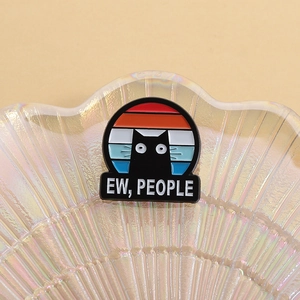 Detail of creative black cat enamel pin with EW PEOPLE text on a shell tray