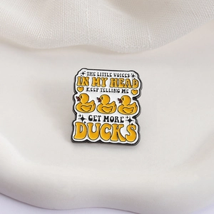 Close-up of enamel pin with yellow ducks and funny quote on a white textured base